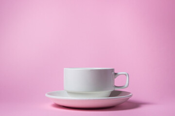 White cup on a pink background. Empty white porcelain cup on a saucer.