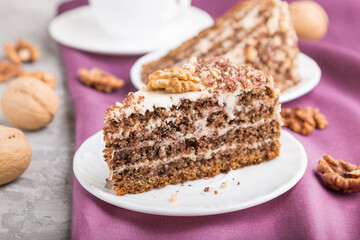 Homemade cake with milk cream and walnuts with cup of coffee on a gray concrete background, side view, selective focus.