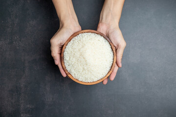 Hands holding a wooden bowl of rice grains for zakat, Islamic zakat concept. Muslims to help the poor and needy. Conceptual shoot for property, income, and fitrah zakat.