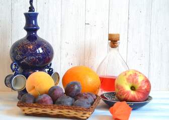 Fruit still life with fresh plums, red apple, orange, peach, a glass bottle with juice and blue...