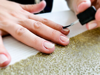 Hands of a female applying transparent nail polish on the nails with a black brush