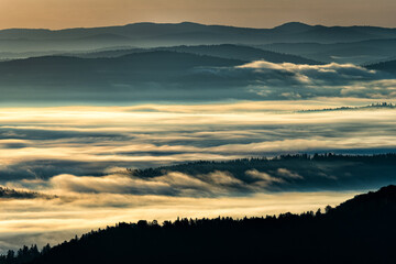 A hazy sunrise in the mountains. Mountains silhouettes and fog in the valleys. Photo from Polonina Wetlinska. Bieszczady National Park. Carpathians. Poland.