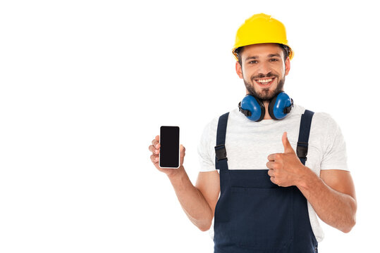 Smiling handyman in workwear showing like gesture while holding smartphone with blank screen isolated on white