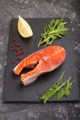 Salmon steak with arugula and lemon on a black slate board on a black concrete background. Side view.