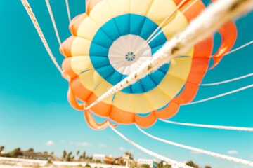 Fototapeta premium Parachute parasailing of tourists on a sandy beach Sunny weather against the background of clear sea and ocean.The wind blows up the canopy of the parachute against a clear blue sky with clouds