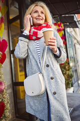 Cheerful female in street in front coffee shop with mobile phone