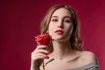 Beautiful girl with bright makeup, holding a rose in her hands on a red background in the studio. The concept of youth, beauty and a healthy body