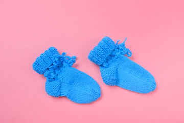 knitted baby booties on pastel pink background.