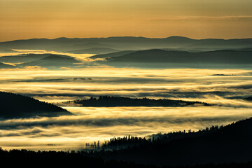 A hazy sunrise in the mountains. Mountains silhouettes and fog in the valleys. Photo from Polonina Wetlinska. Bieszczady National Park. Carpathians. Poland.