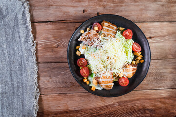 Appetizing Caesar salad with chicken in a black plate on a wooden table. The concept of healthy food and serving