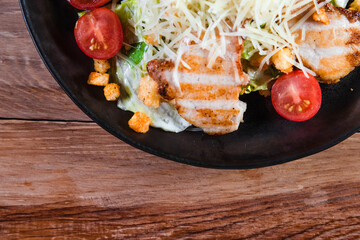 Appetizing Caesar salad with chicken in a black plate on a wooden table. The concept of healthy...