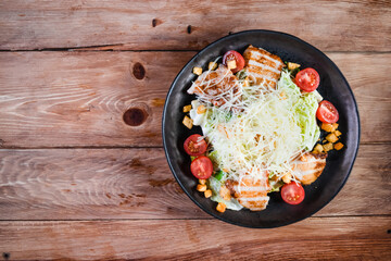 Appetizing Caesar salad with chicken in a black plate on a wooden table. The concept of healthy food and serving