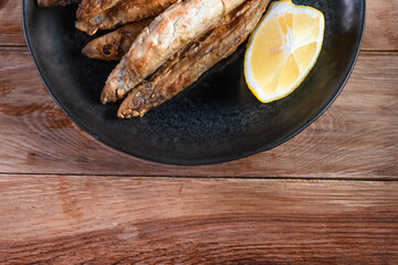 Appetizing fried capelin on a black plate stands on a wooden surface. Simple rustic food concept