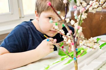 Spring theme. Boy making flowering apple tree garden layout. Recycling concept. Trees made of tree branch and styrofoam.