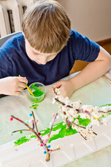 Spring theme. Boy making flowering apple tree garden layout. Recycling concept. Trees made of tree branch and styrofoam.