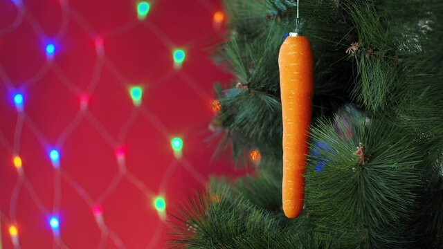Vegan Christmas concert. Tree is decorated with fresh vegetables. raw carrots on a pine branch on a red background with bokeh. idea of minimalism and eco-friendly celebration without waste. Copy space