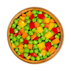 Green peas and diced bell peppers in wooden bowl. Mixed vegetables. Seeds of pod fruit Pisum sativum and cut yellow, orange and red sweet peppers, Capsicum annuum. Closeup from above macro food photo.