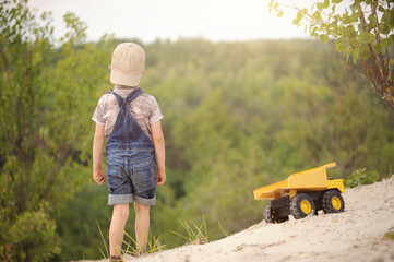 Child, little boy have fun with toy excavator and dumper in the sand. Carefree childhood.