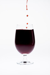 Red wine being poured into wine glass on white background.