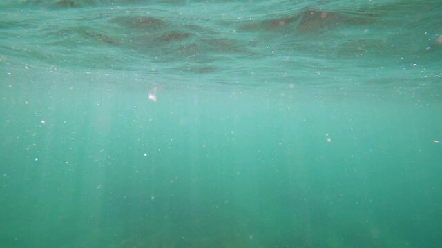 Waves underwater with bubbles and sun rays. Blue ocean in underwater