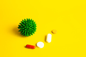 COVID-19 on a yellow background. New coronavirus infection. Image of a green coronavirus. Tablets, antibiotics against the disease of pneumonia and cough.