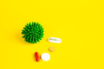 COVID-19 on a yellow background. New coronavirus infection. Image of a green coronavirus. Tablets, antibiotics against the disease of pneumonia and cough.