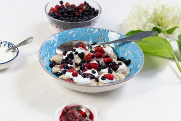 Bluberry and wild strawberry sweet dumplings vareniki with sour cream  in plate with spoon on white wooden background with hydrangea flower
