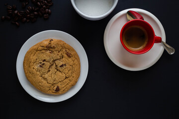 Chocolate chip cookie with red espresso cup and coffee beans on black background