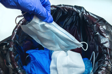 Hand in medical gloves throwing out discarded, used protective masks in the trash bin after quarantine