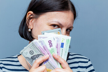 woman covers face with banknotes on the gray background