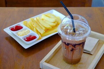 Iced chocolate marble drink served in plastic glass with crispy French fries and sauce on wood table
