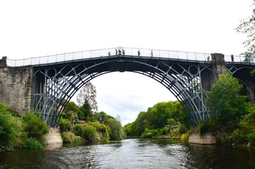 A view of the first cast Iion Bridge at Ironbridge, spanning the River Severn,  from low level along the river with bushes and trees on either side