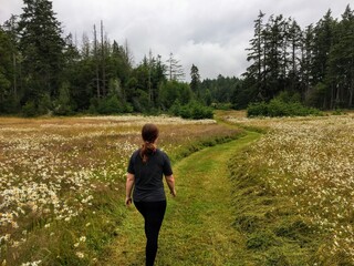 A young female hiker walking through the meadows of East Sooke Regional Park, surrounded by forest.  On Vancouver Island, British Columbia, Canada.