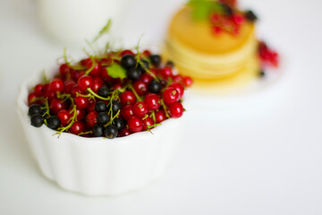 
Ripe red and black currants in a white bowl on a white background, healthy summer breakfast with berries.