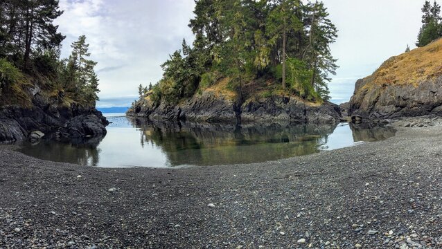 A wide lengthened view of a beautiful bay with a rocky beach and beautiful island, This is the east sooke coast trail, outside Sooke, British Columbia, Canada