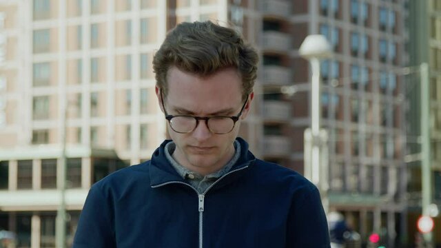New generation caucasian looking down on his phone middle of downtown navigating modern lifestyle 5g