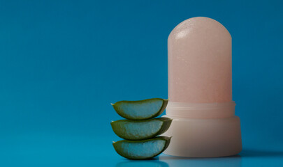 Natural crystal alum deodorant and fresh aloe on a blue background. Space for text.