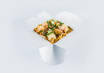 Isolated Food delivery box with ready meals inside. Asian Seafood Udon Wheat Noodles with shrimp, mussels, calamari, scallop, vegetables and spring onion scallions in white carton takeaway package.
