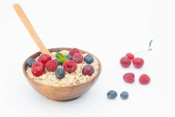 Rolled oats with blueberries and raspberries on white background. Healthy breakfast cereal oat flakes in wooden bowl with wooden spoon.