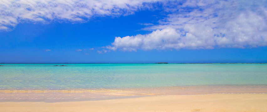 Beach with pink sand and turquoise water and clouds in blue sky.