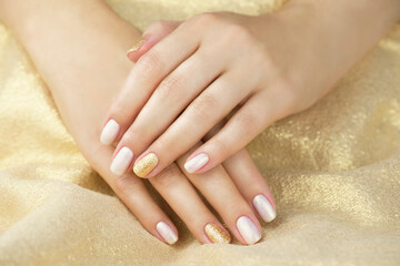 Golden manicure on a golden background. Manicure with white and yellow gold color.