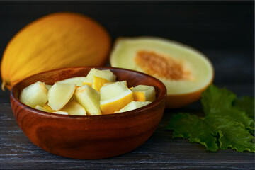 slices of cut melon in a wooden bowl close-up. background with melon slices in a bowl and a whole melon on the table.