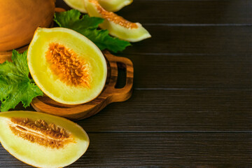 half a fresh melon and slices of melon in a wooden bowl on the table above. background with fresh melons on the table close-up. yellow melons and green leaves top view.