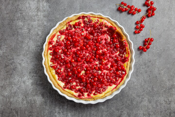 Redcurrant cheesecake, tart with fresh berries in a white baking dish. Dark gray background. Top view.