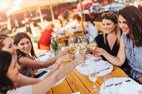 Young female friends clinking glasses with wine on the summer terrace of cafe or restaurant