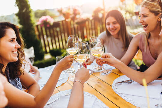 Young female friends clinking glasses with wine on the summer terrace of cafe or restaurant