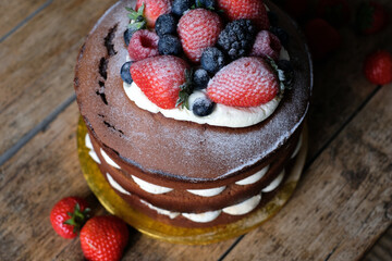 Delicious homemade cake with blueberries, raspberries, blackberries, strawberries and cream on the wooden background