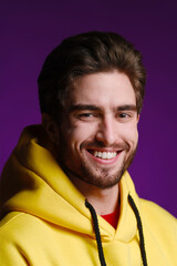A young man of 25-30 years in yellow sweatshirt emotionally poses on a purple background. 