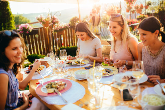 Young beautiful female friends are talking, eating, drinking and smiling while sitting at the table and having lunch