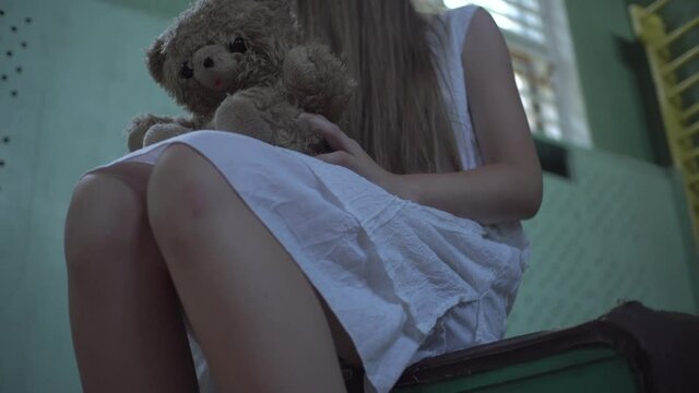 A girl is sitting in a white sundress in an old abandoned school gym. hair on his face, a toy in his hands. Horror.Abandoned house. Mysticism.